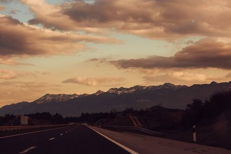 mountainous winding road in the background of mountains and sky with cloudsの写真素材