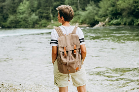 girl tourist backside with backpack on the bank of a mountain river on a sunny day