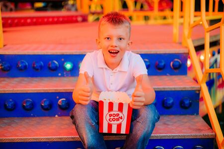 popcorn and child with emotions of joy and signs on the fingers like a carousel outside festival fair with colorful backgroundの写真素材