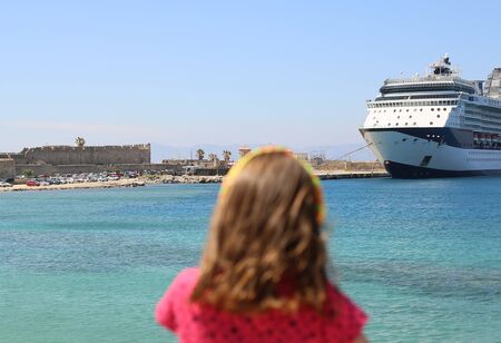 little girl outside in a red dress looks cruise liner moored on a pierの写真素材