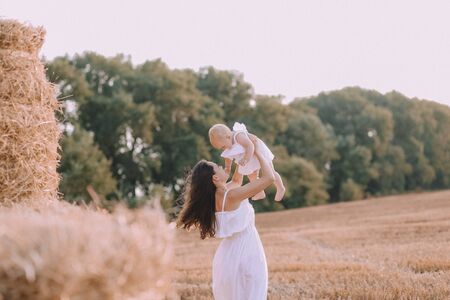 autumn conceptual mother with a small daughter in white dresses on a field with a strawの写真素材