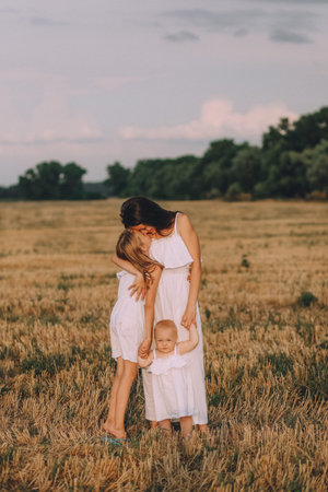autumn conceptual mother with a small daughter in white dresses on a field with a straw