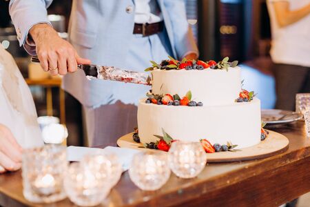 man slices a festive fruit cake and a knife all in creamの写真素材