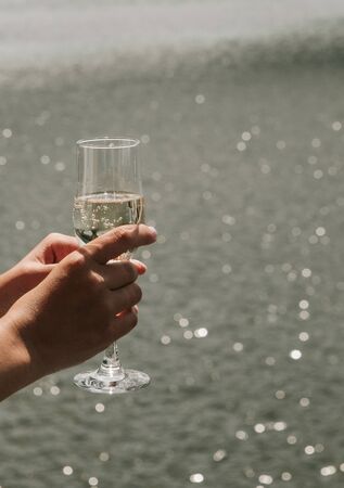 glass with champagne in hands on a background of sea water conceptualの写真素材