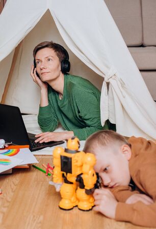 mom works laptop headphones music sound isolation child next plays with a robotの写真素材