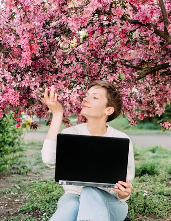 woman with laptop connection with smile relax outside park sakura bloom pinkの写真素材