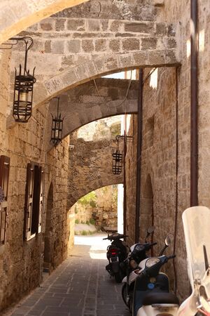 scooters parking on a narrow city street with stone ancient buildingsの写真素材