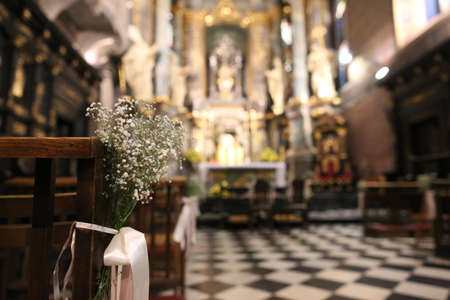 white flowers on a bench in majestic architecture of the catholic cathedral inside with columnsのeditorial素材