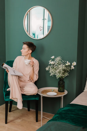 morning women in armchair with cup of tea and fashion magazine bedroom and pajamas