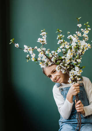 happy child girl with tree flowers playfully hiding behind branchesの写真素材
