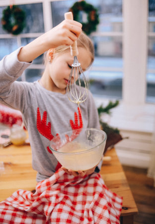 girl whips an egg white with a whisk to make cookies on the background of a christmas tree