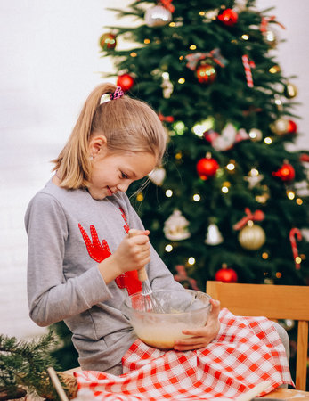 girl whips an egg white with a whisk to make cookies on the background of a christmas tree