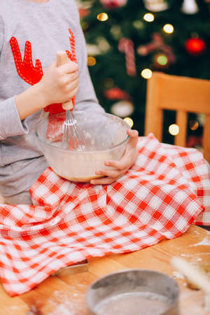 girl whips an egg white with a whisk to make cookies on the background of a christmas treeの写真素材