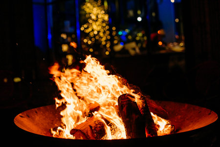 night bonfire in metal bowl stand flaming sparks and garlands background