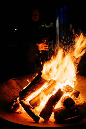 night burning bonfire on a metal stand and a man throws a log