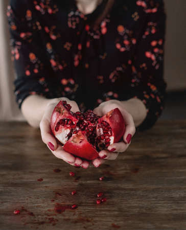 opened ripe fruit red pomegranate in the hands of a woman at the tableの写真素材
