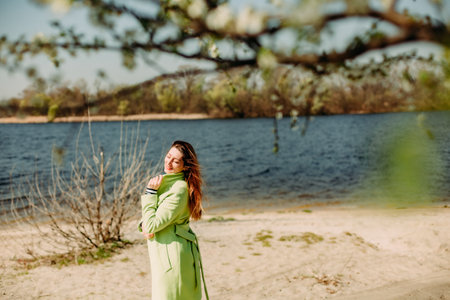 stylish woman in a green coat on the background of spring flowering and the riverの写真素材