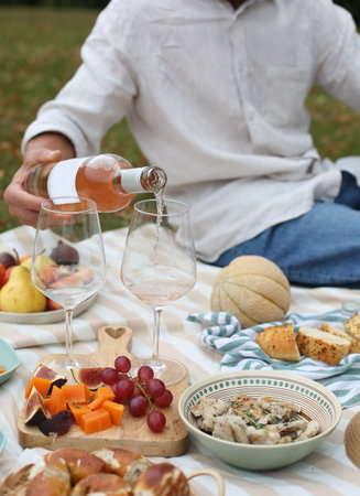 A cozy summer picnic setup with rosÃ© wine being poured into glasses, surrounded by fresh fruits, cheese, bread, and light snacks on a blanket in the park. Relaxed outdoor dining and lifestyle concept.の写真素材