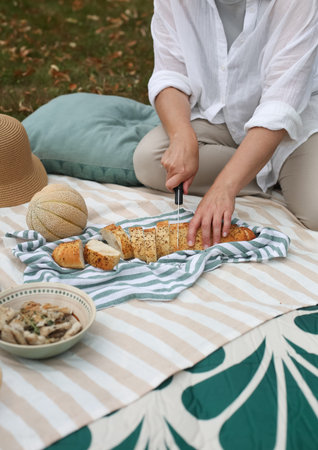 A woman in a hat sitting on a picnic blanket with a glass of rosÃ© wine, surrounded by fruits,...