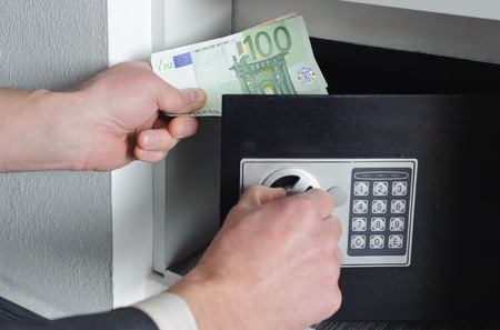 Man with one hand opens the safe  and the other holds moneyの写真素材