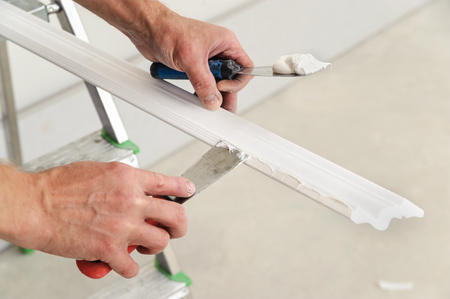 Installation of ceiling moldings. Worker puts glue on plastic molding for further fixing it to the ceilingの写真素材