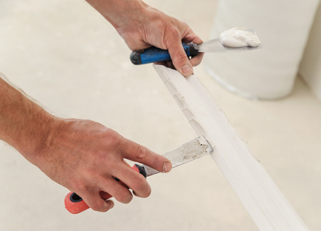 Installation of ceiling moldings. Worker puts glue on plastic molding for further fixing it to the ceilingの写真素材