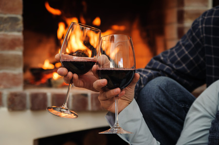 Two glasses of wine in the hands of man and woman on the background of fireの写真素材