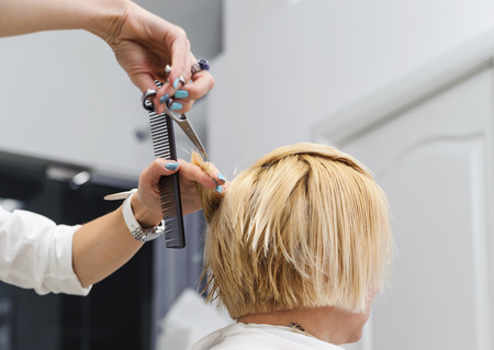 Hairdresser cutting blonde hair with scissorsの写真素材