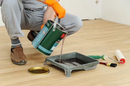 Lacquering wood floors. A worker pours floor lacquer in the tray.の写真素材