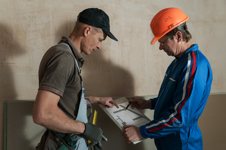 Worker and foreman discuss the scheme plasterboard ceiling in the drawingの写真素材