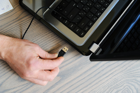 The hand of man connects the USB cable to the laptop. Top view.の写真素材