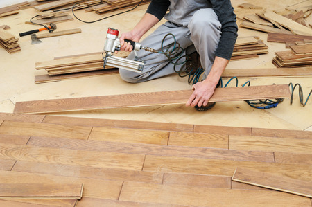Installing a wooden floor. A worker fixes the board using a nail gun.の写真素材
