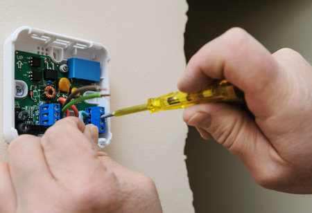 Installing a programmable room thermostat. Man's hands fixing the wires to the terminals and...