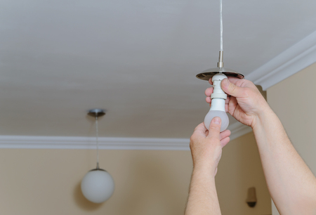 Electrician's hands are installing a LED light bulb in a lamp.の写真素材