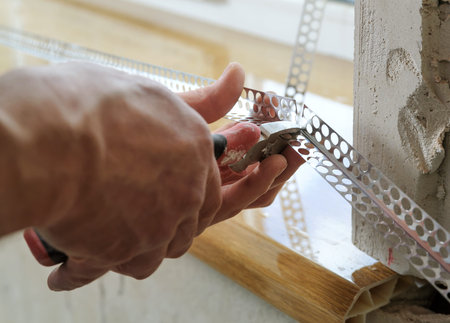 Worker's hands are cutting a perforated aluminum corner for installation on an external the angle.