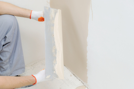 Woker's hands are holding a long trowel with a putty.の写真素材