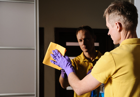The man cleans the mirror in the house. He wipes the glass with the rag.の写真素材