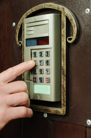 Man's hand is dialing the code on the door intercom of the front door.