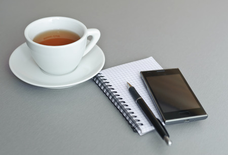 Smartphone, notebook, pen and cup of tea on a gray backgroundの写真素材