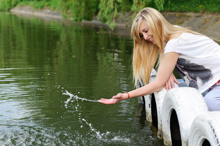 Young beautiful woman sitting on the pier bent to the water. She plays with splashesの写真素材