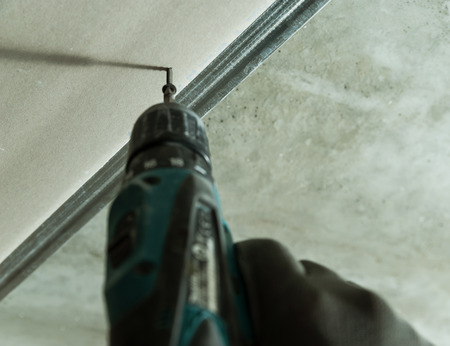 Man fixes the drywall to metal frame using screwsの写真素材