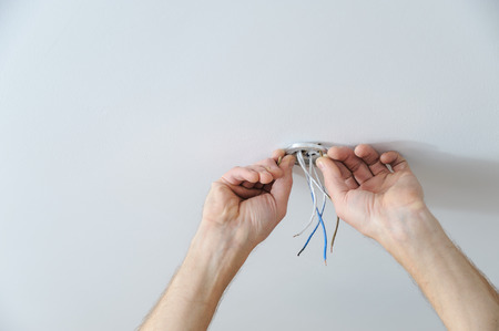 Installing a spotlight in the room. The  man's hands is fixing the bracket for the ceiling lamp.の写真素材