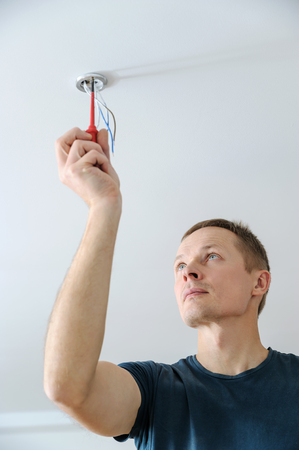 Installing a spotlight in the room. The man is fixing the bracket for the ceiling lamp.の写真素材