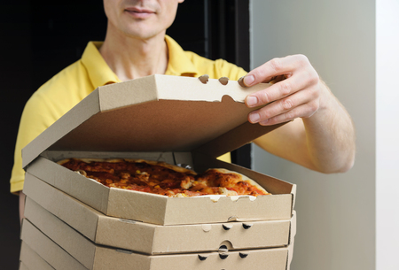 Food delivery home.  The man is holding boxes with pizzas in the doorway. The top box has been opened.の写真素材