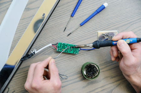 The man is repairing the power supply of the lamp. He is holding an electronic board and a soldering...