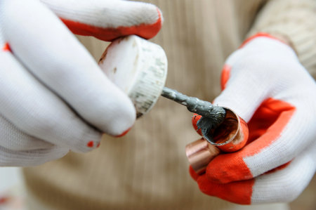A worker is applying flux to the inside of the socket of the copper tube.