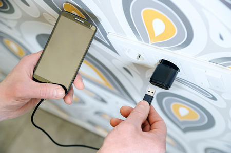 A man is inserting a power cord into a USB power supply for charging a smartphone.の写真素材
