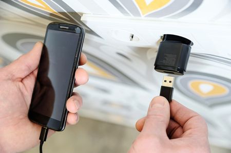 A man is inserting a power cord into a USB power supply for charging a smartphone.の写真素材
