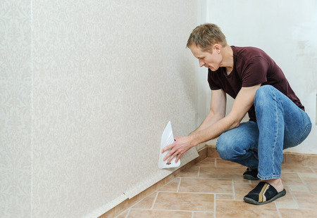 Glueing wallpapers at home. Man  is using scraper to smoothing wallpapers on the wall.の写真素材