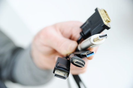 There are various cords and plugs in the hand of a man.